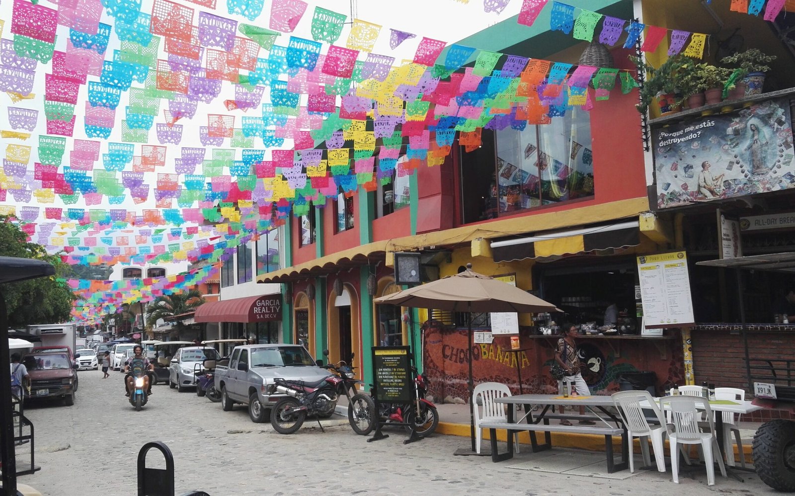 street decorated with colourful flags cafes and cars line the streets
