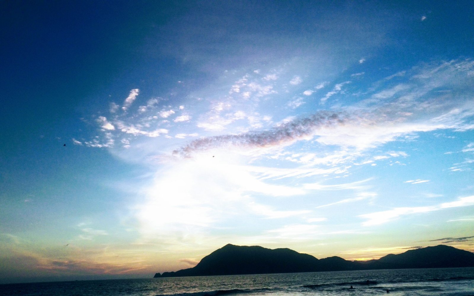 colourful sky with a stroke of clouds sunset over ocean and a little island mountain